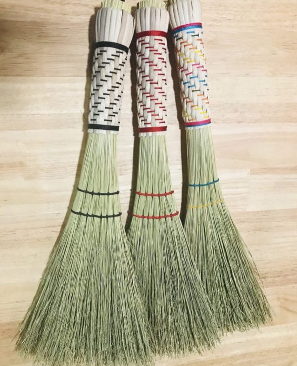 3 Whisk Brooms against a light wood floor.